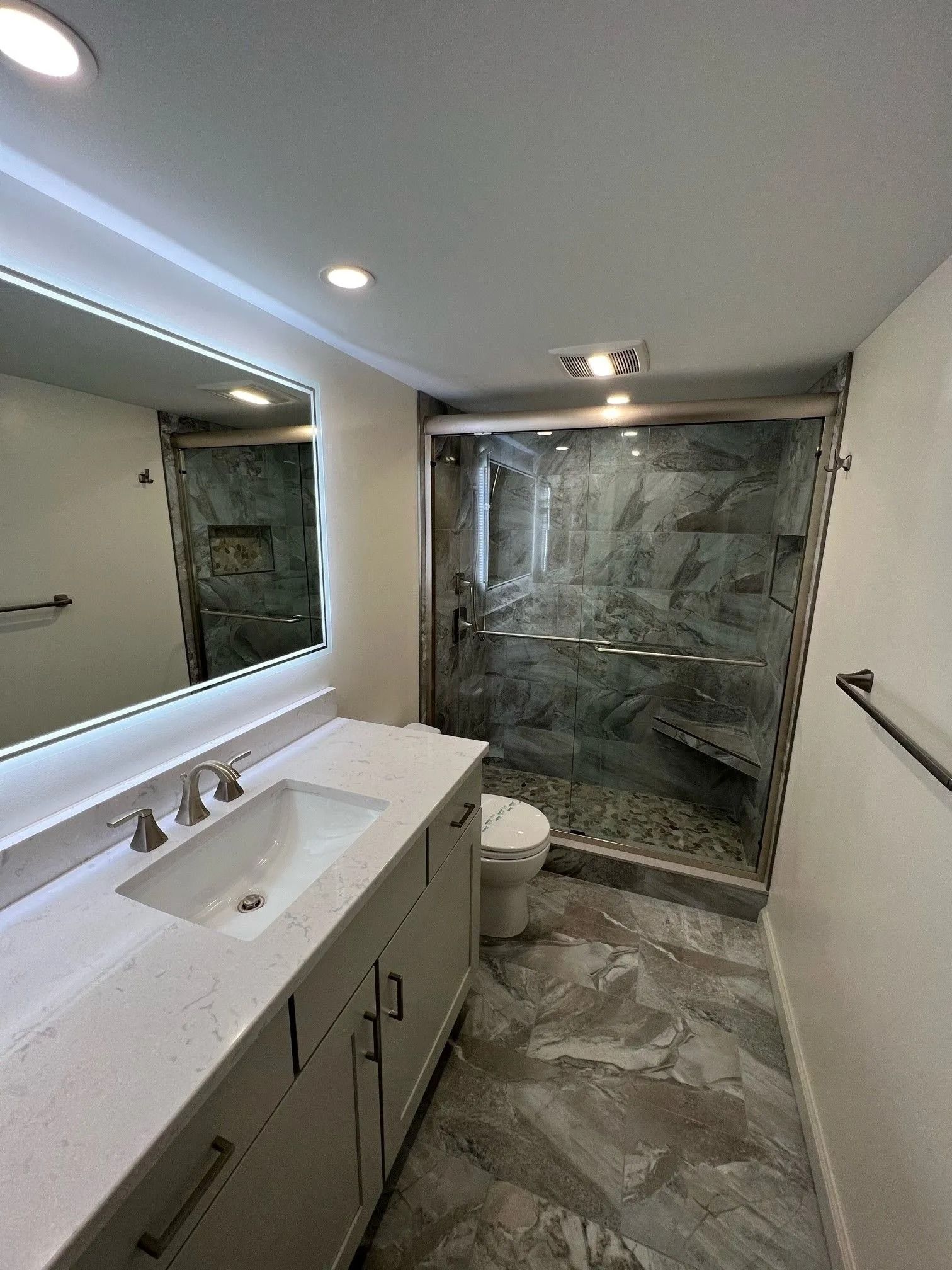 Modern bathroom with double vanity, large mirror, and glass-enclosed shower with marble tile.