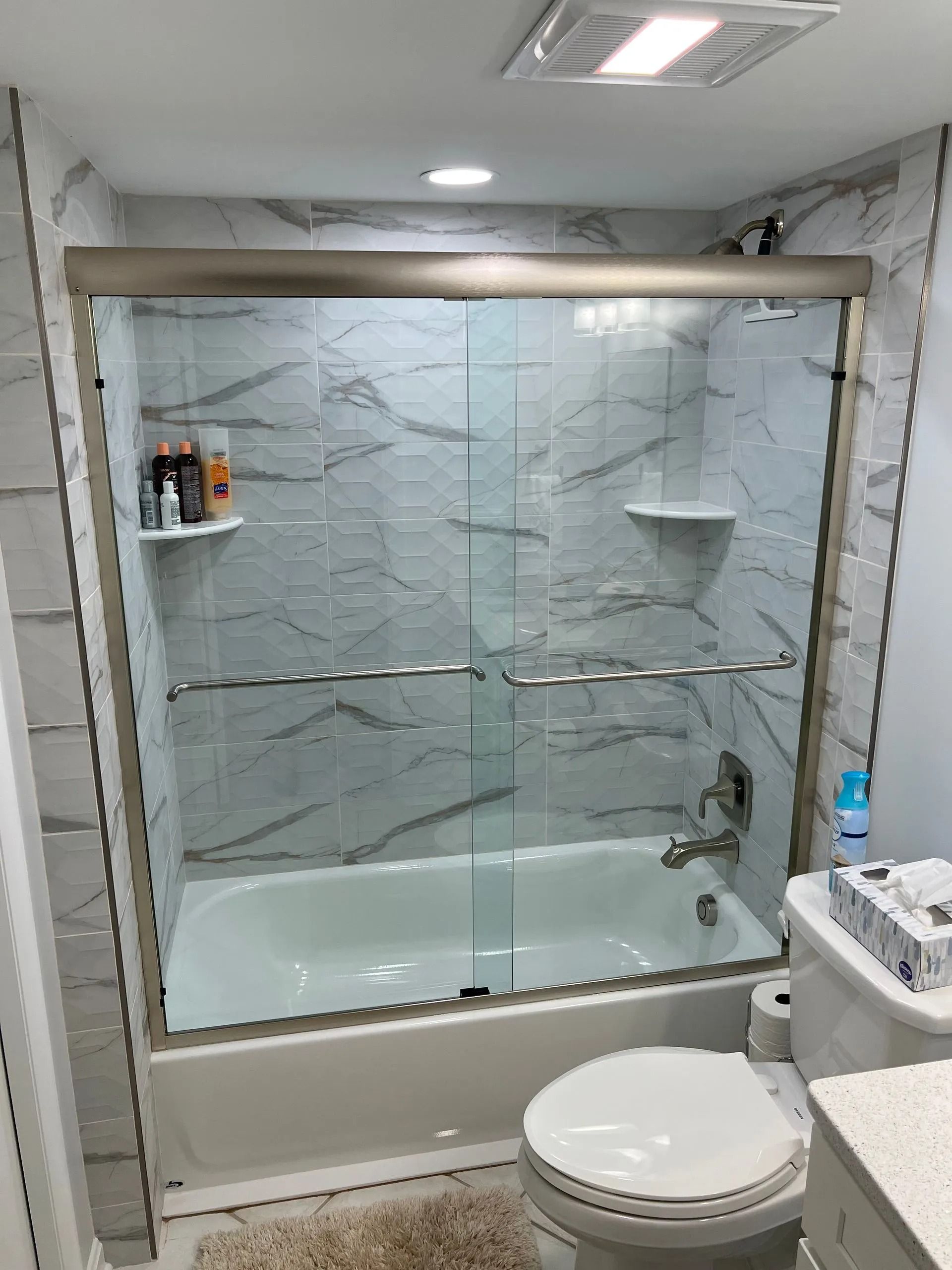 Bathroom with glass-enclosed bathtub shower, white tile, and toilet in the foreground.