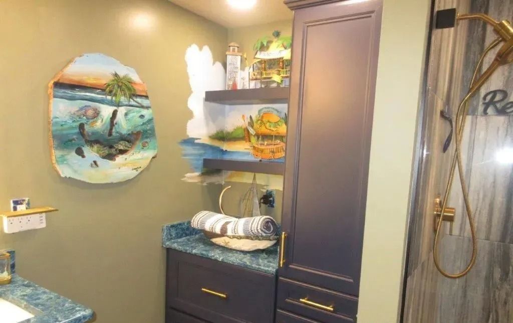 Bathroom with vanity, tall cabinet, shower, and beach-themed wall art in warm lighting