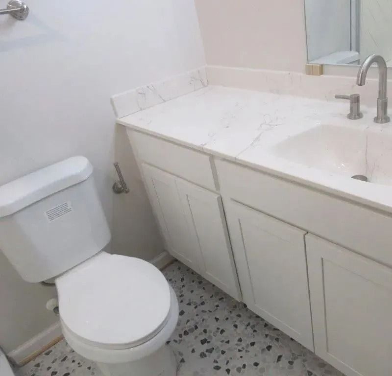 Small white bathroom with toilet, marble vanity, and sink with mirror.