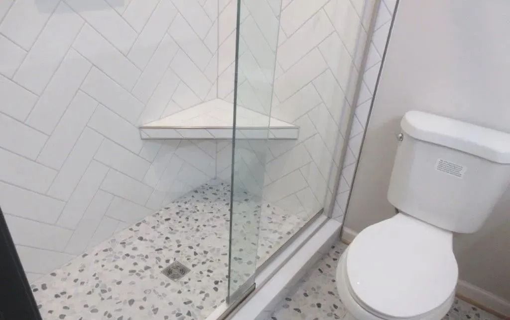 Small white bathroom with a walk-in shower, glass door, and toilet on speckled tile floor