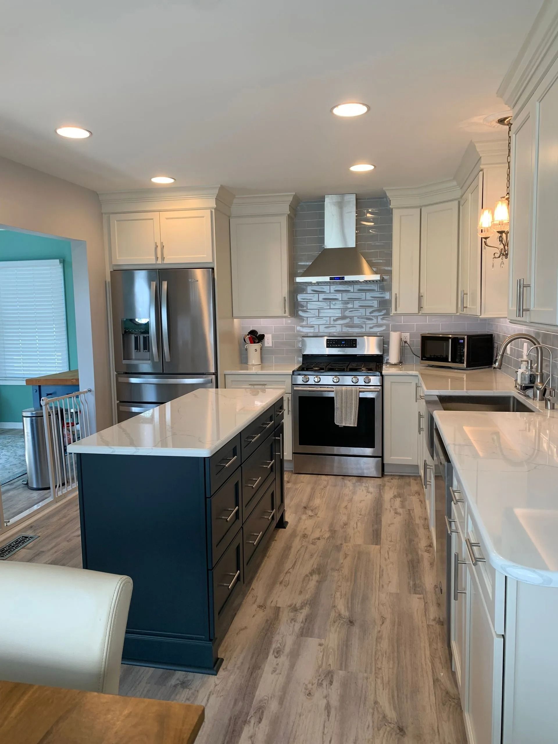 Bright modern kitchen with white cabinets, island, stainless steel appliances, and wood-look flooring