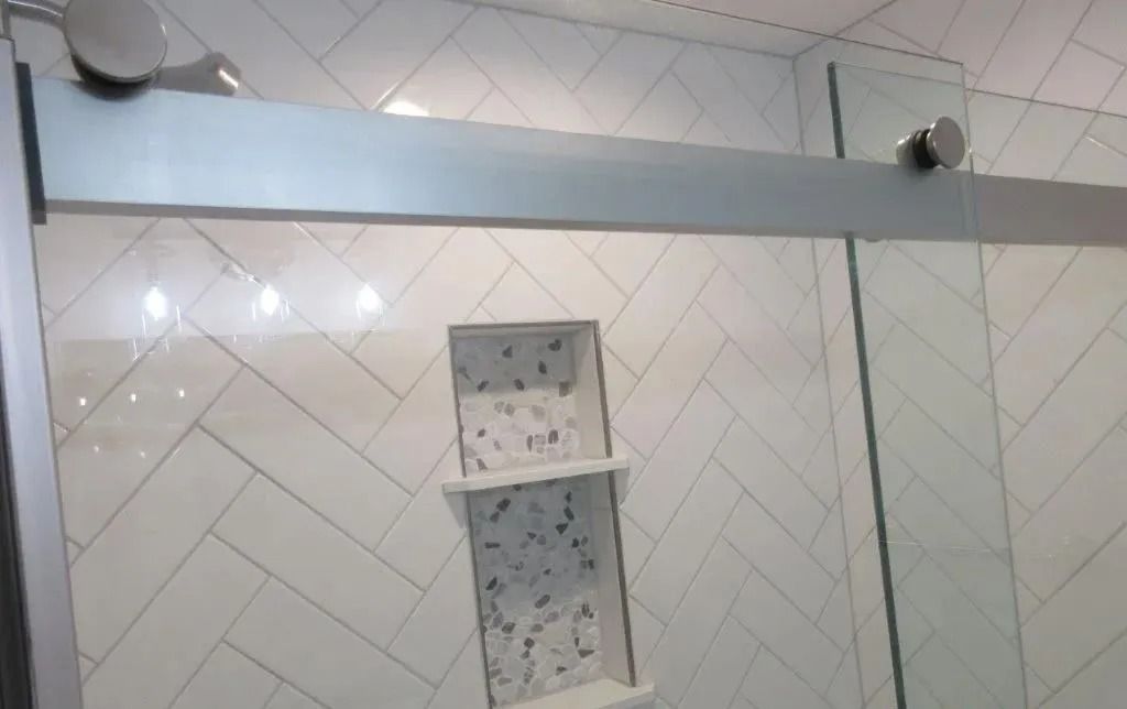 Bathroom shower wall with white tiles, a built-in shelf niche, and a glass shower door panel