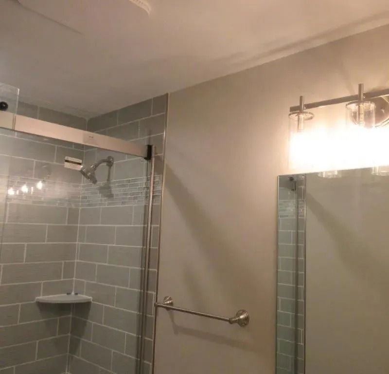 Bathroom with gray tiled shower, wall mirror, and vanity light.