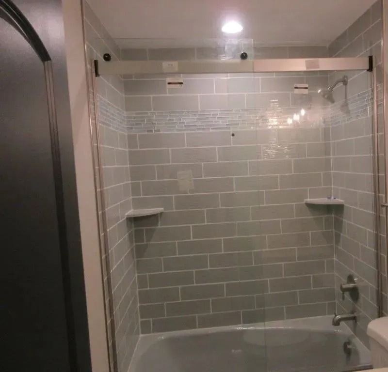 Bathroom with gray tile shower, tub, glass door, and white shelves under a towel bar.