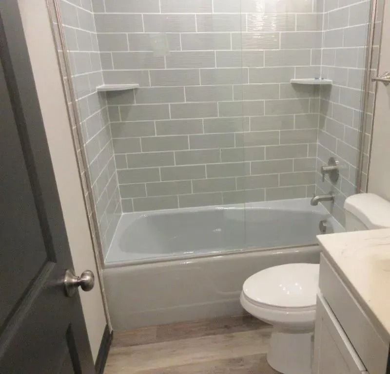 Small bathroom with a bathtub-shower, white tile walls, toilet, and vanity sink.