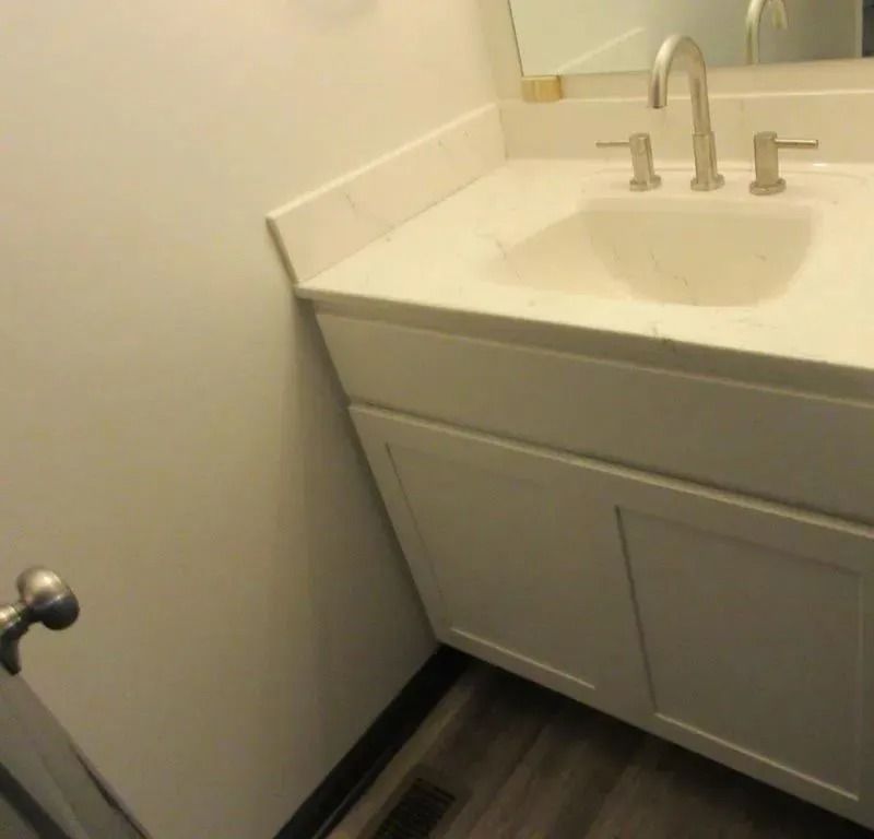 Small bathroom vanity with white sink, cabinet, and mirror on a dark wood floor