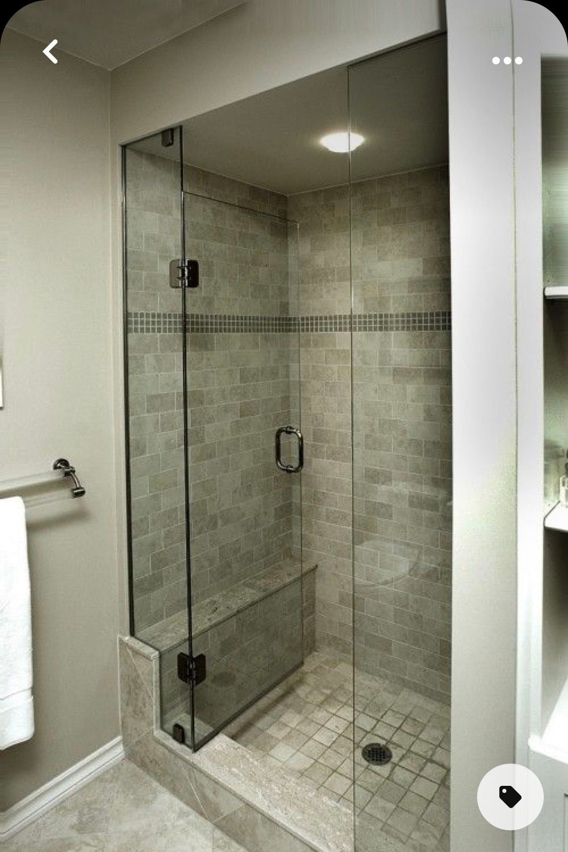 Glass-walled tiled shower with a bench and handheld showerhead in a modern bathroom