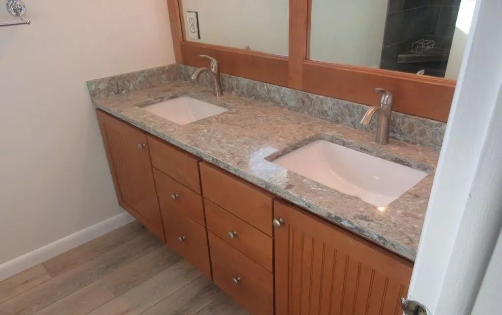 Double vanity bathroom with granite countertop, two sinks, and wood cabinets beside a large mirror