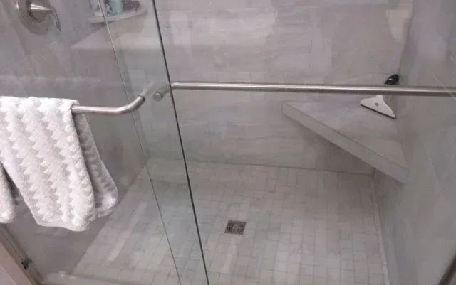 Glass shower with tiled floor, grab bars, and a towel hanging nearby