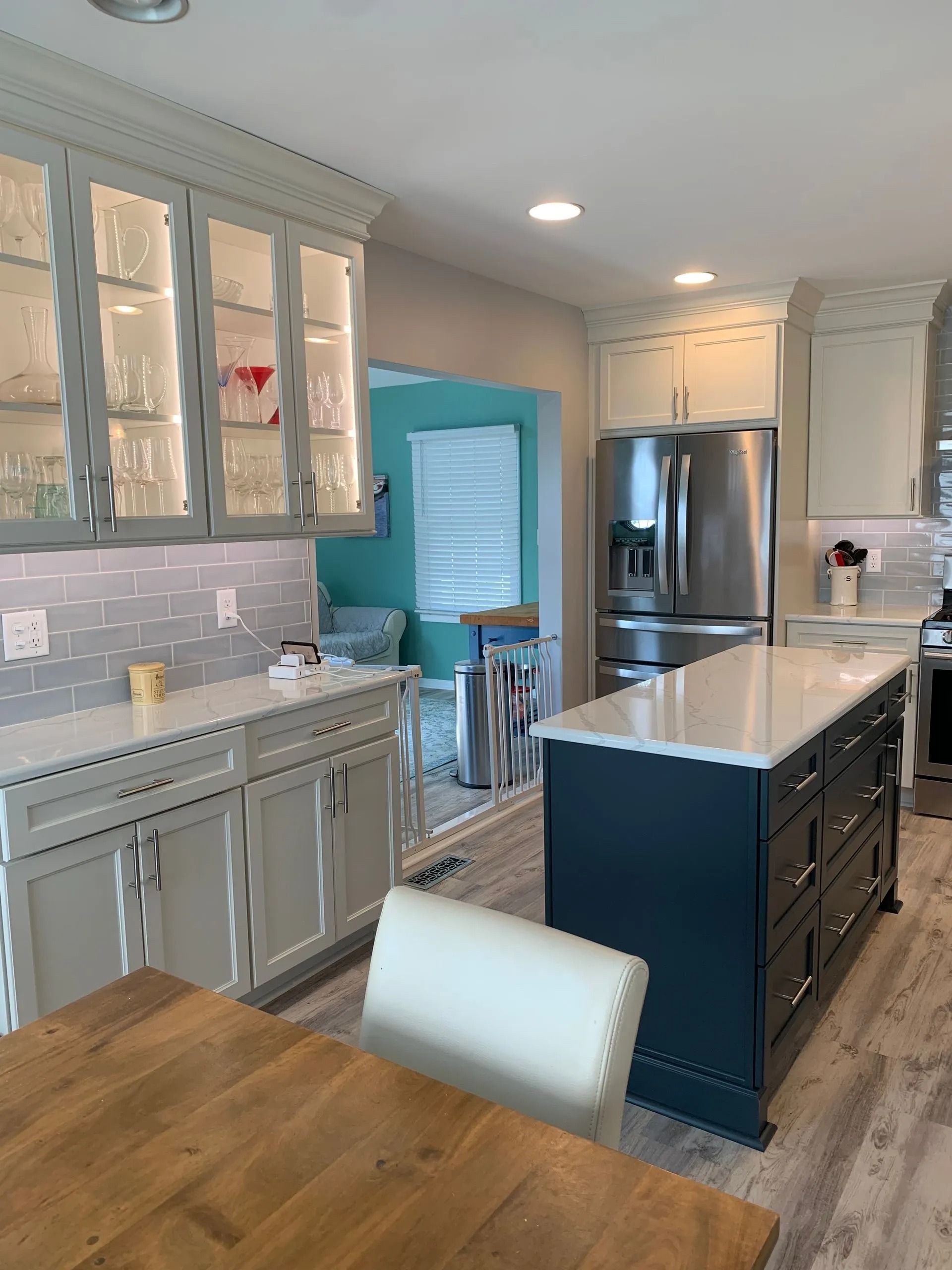 Bright kitchen with white cabinets, teal island, stainless steel fridge, and wood dining table.
