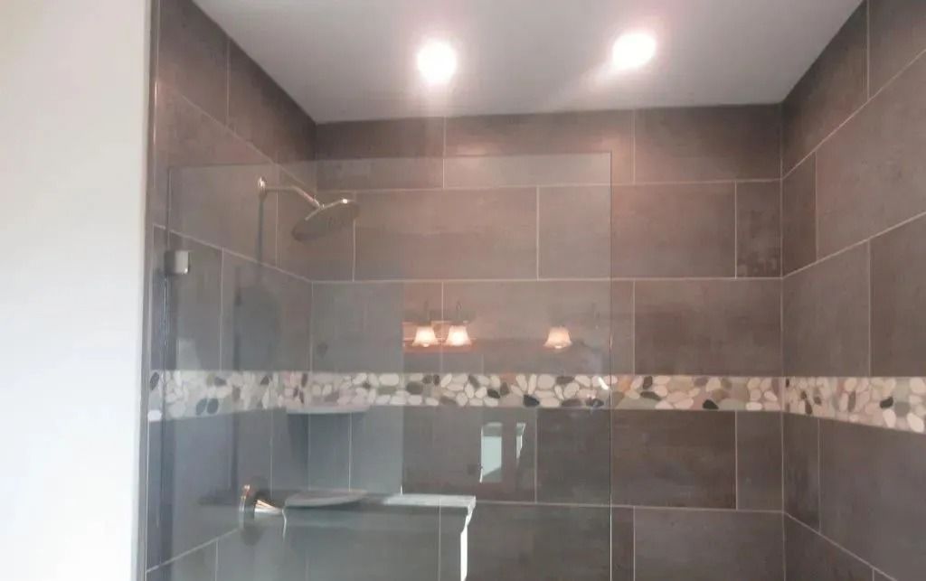 Modern bathroom shower with gray tile walls, glass enclosure, and recessed ceiling lights