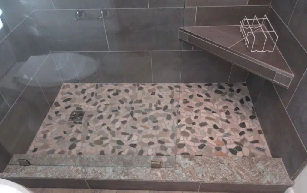 Empty tiled shower with pebble floor and a corner shelf