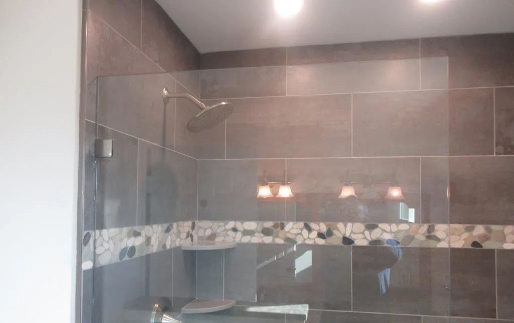 Modern shower with gray tile walls, glass enclosure, and decorative mosaic border.