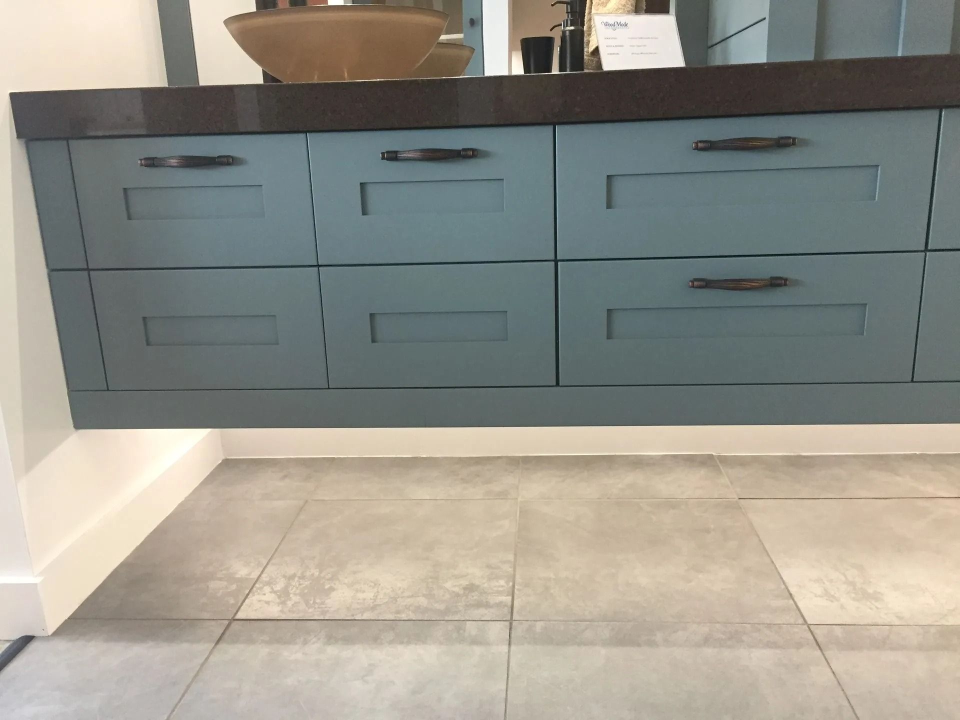Gray bathroom vanity with six drawers and a dark countertop above large beige floor tiles