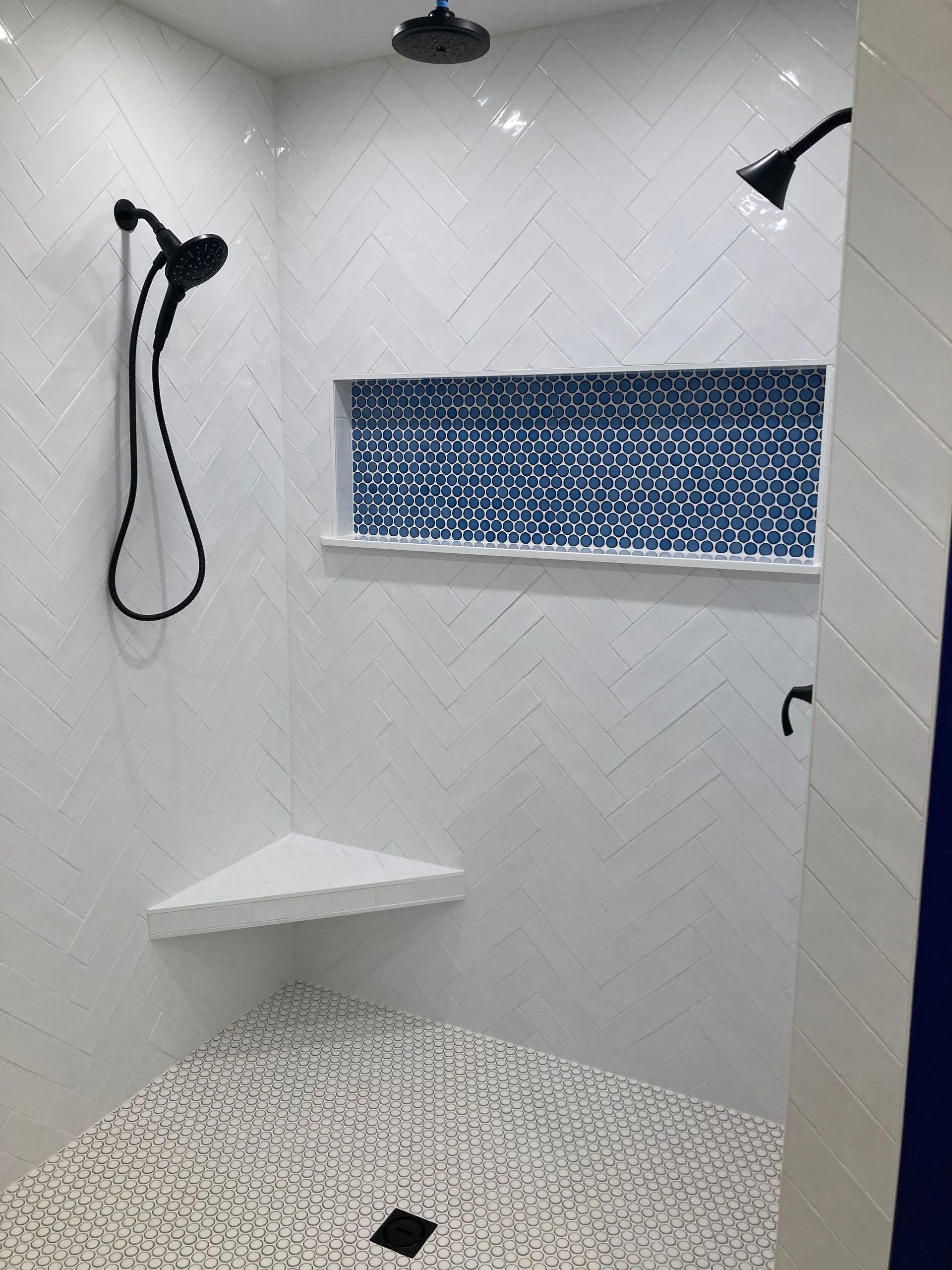 Walk-in shower with white tile, black fixtures, a bench, and a blue-patterned recessed shelf.
