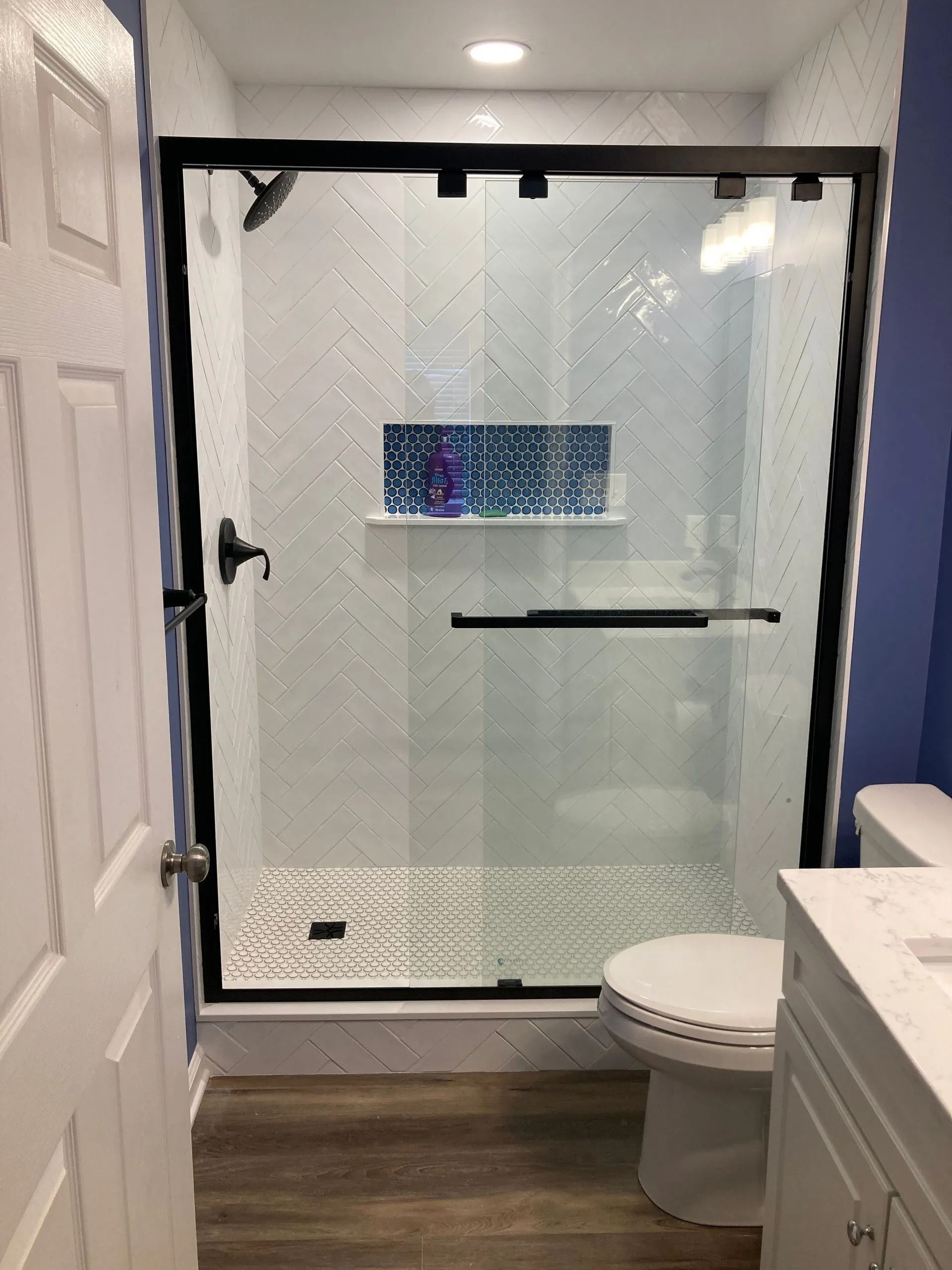 Modern bathroom with a glass shower, patterned tile walls, and a toilet beside a vanity.