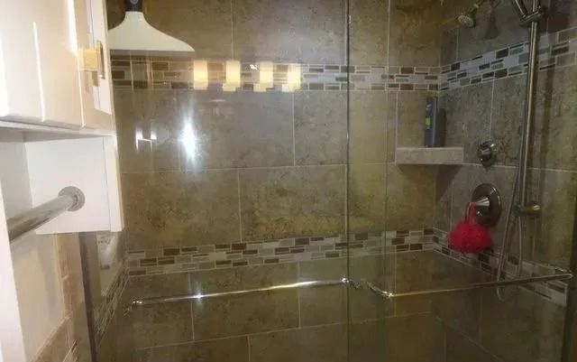 Glass-enclosed tiled shower with shelves, a towel rack, and a red hanging item