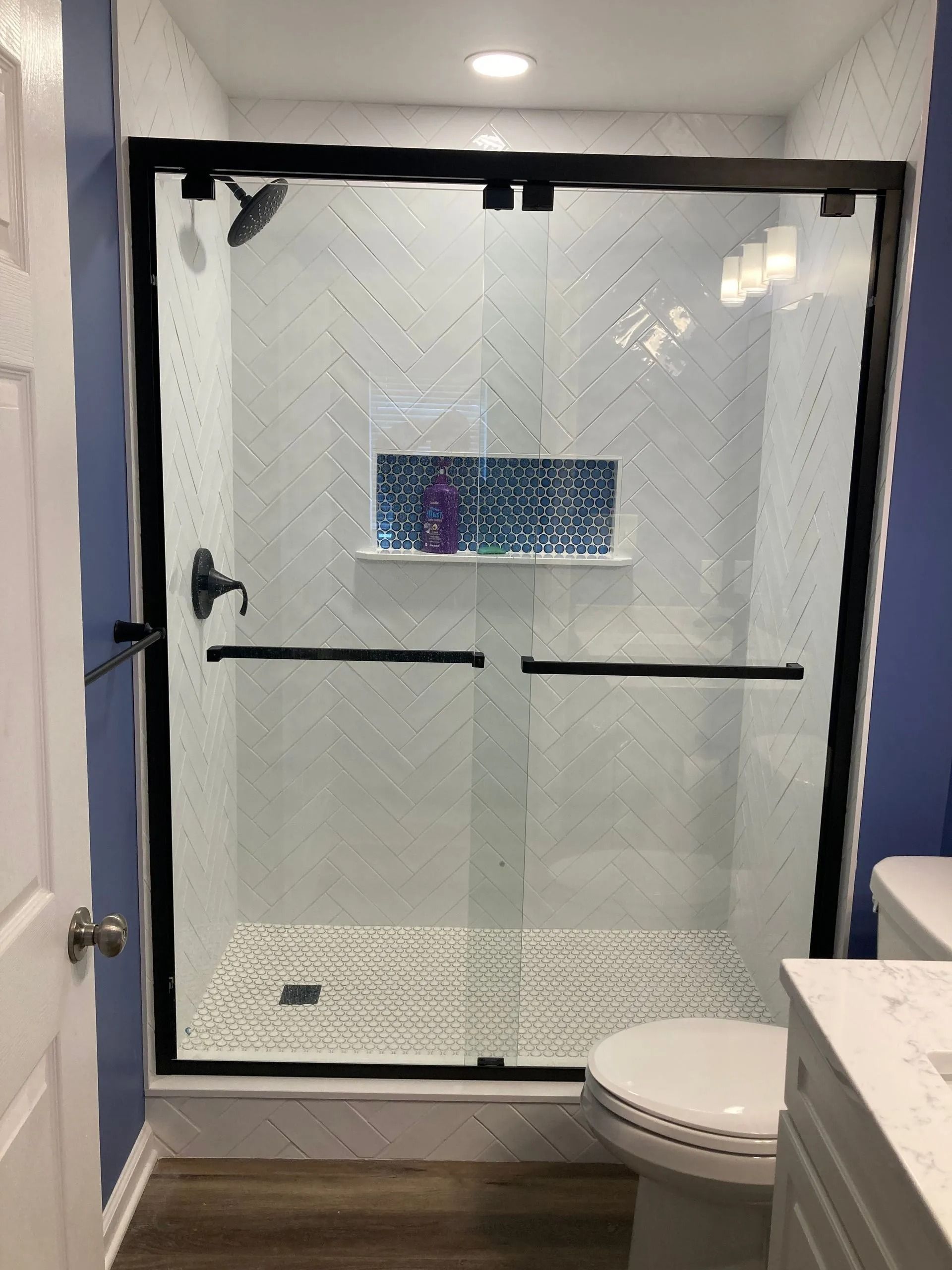 Glass shower enclosure with white herringbone tile and black trim in a bathroom