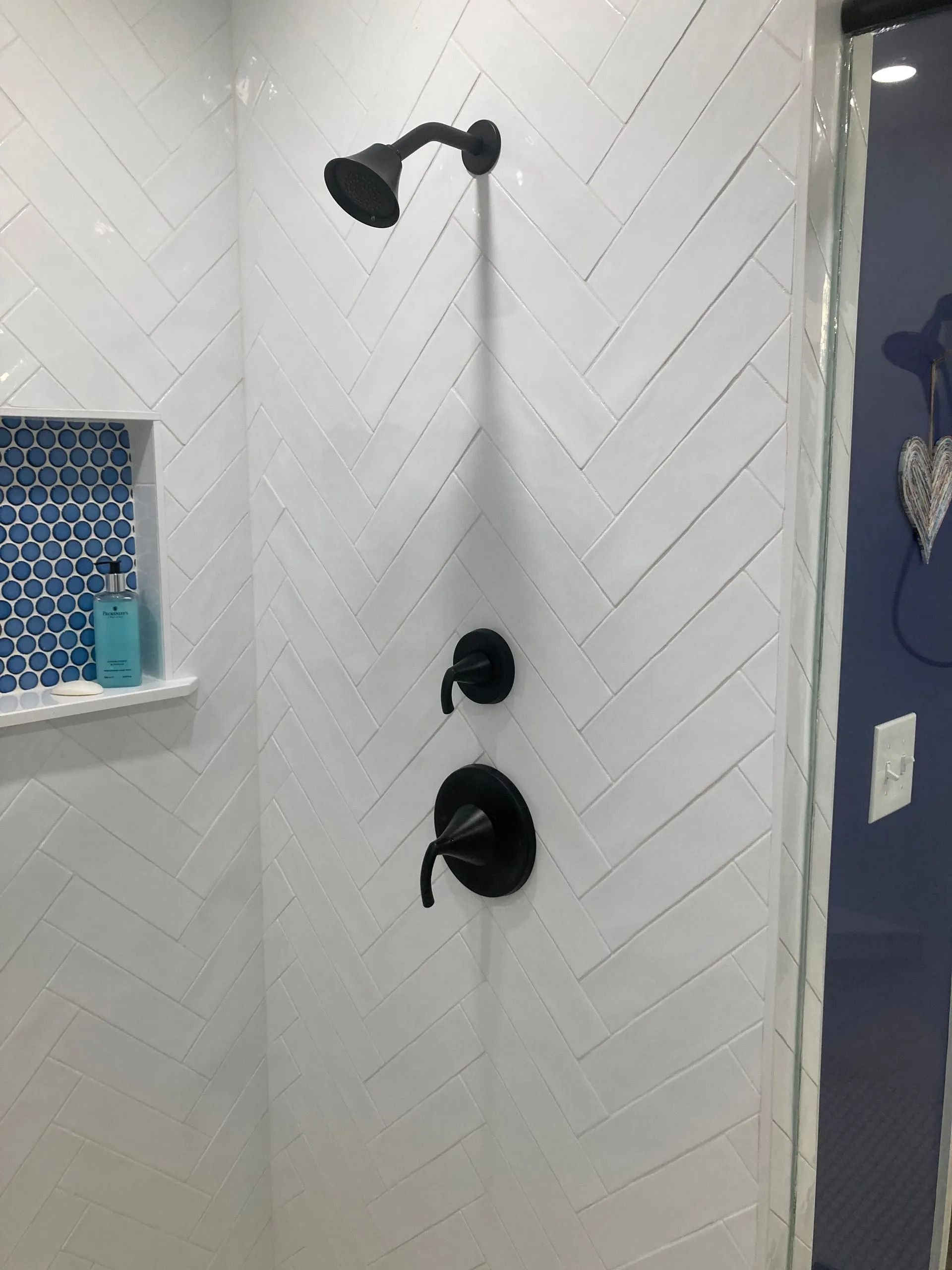 Black shower head and fixtures on a white tiled bathroom wall, with a tiled niche and dark blue accent wall.