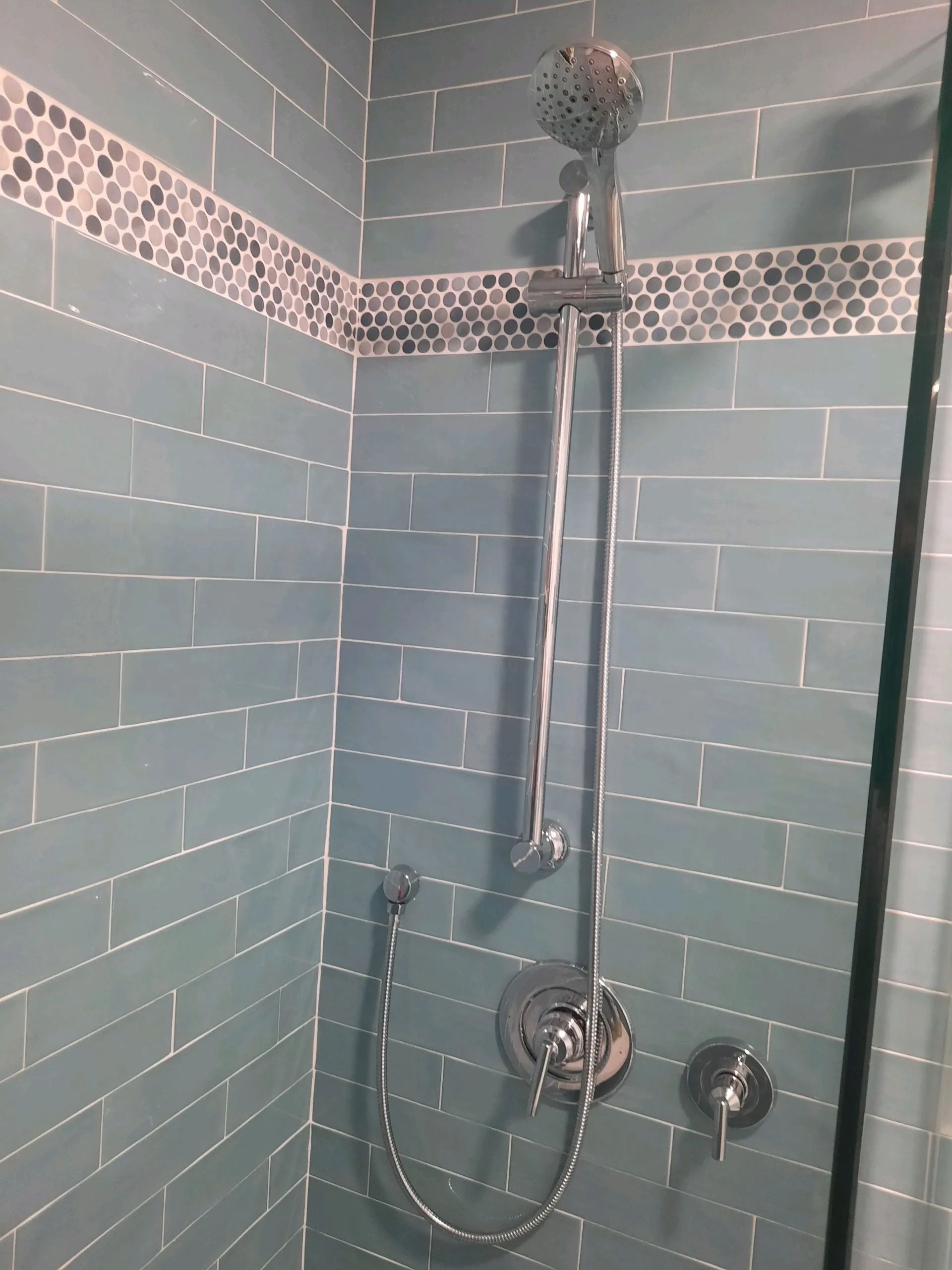 Blue tiled bathroom shower with handheld showerhead, grab bars, and mosaic accent strip