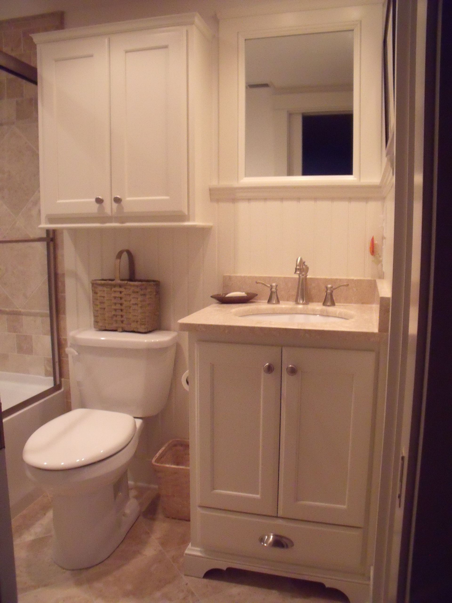 Small bathroom with white toilet, beige vanity, and mirror cabinet beside a tiled wall.