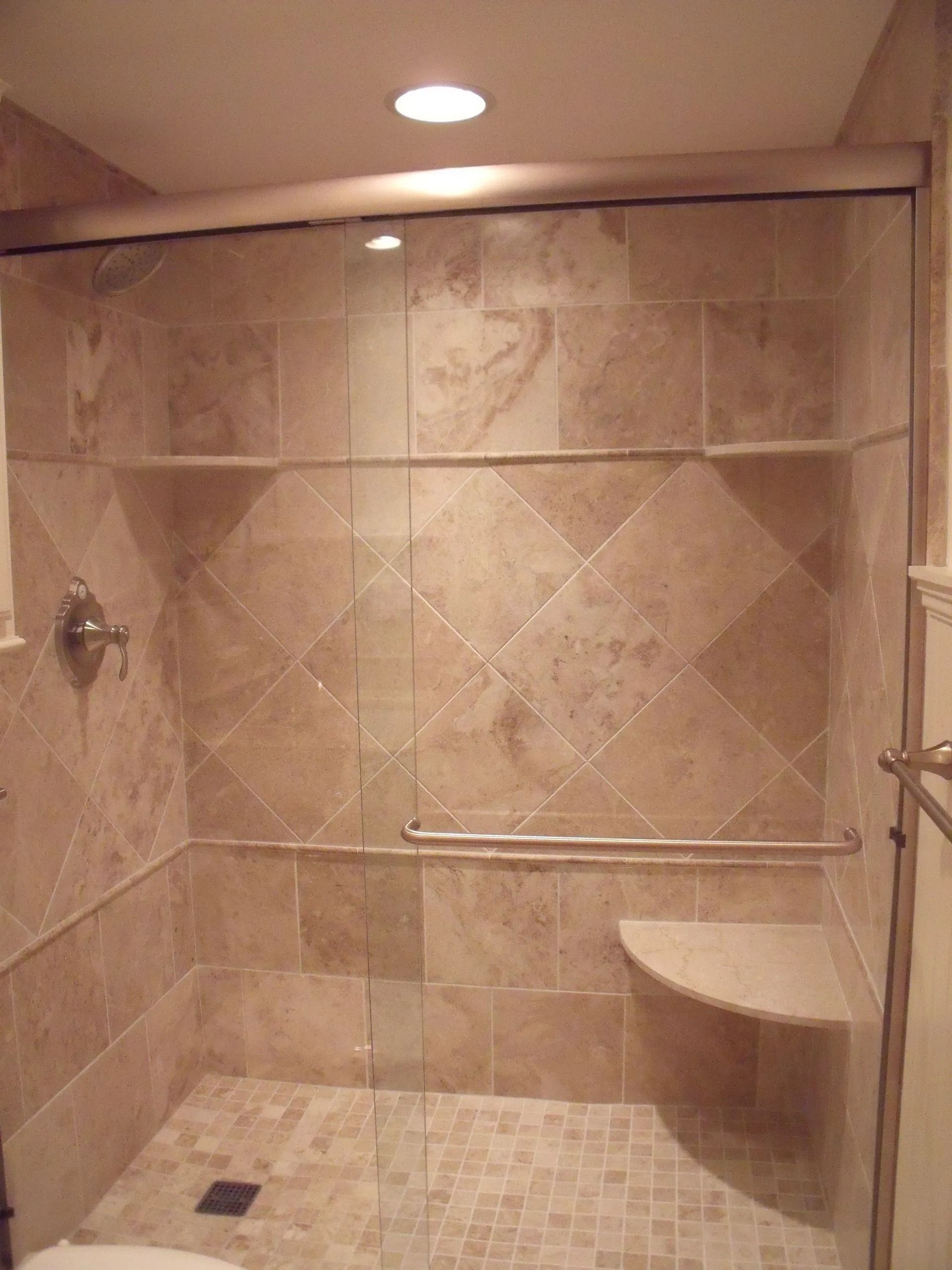 Small tiled shower stall with glass door, built-in bench, and overhead light.