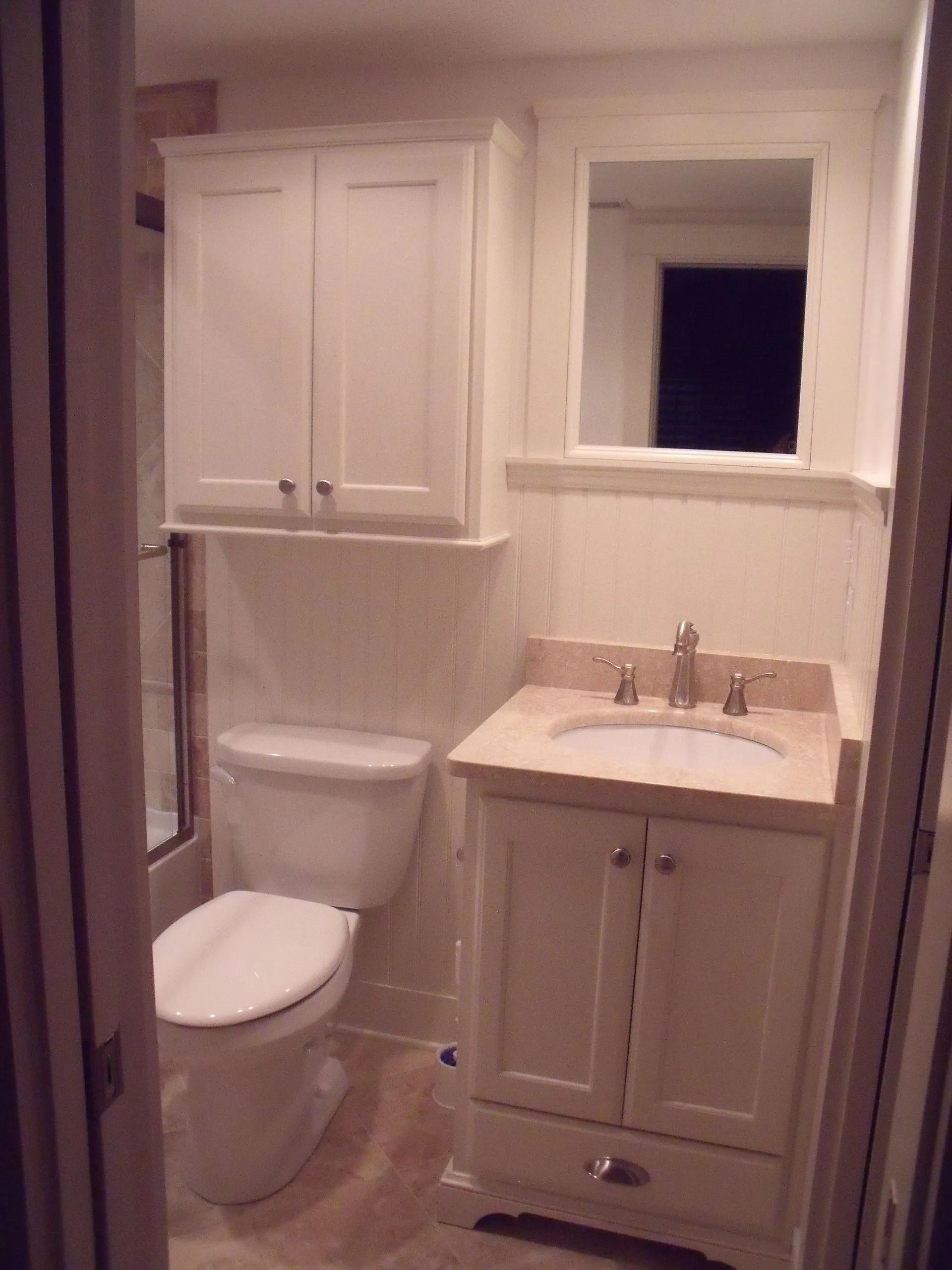 Small bathroom with white toilet, sink cabinet, and window above the sink.