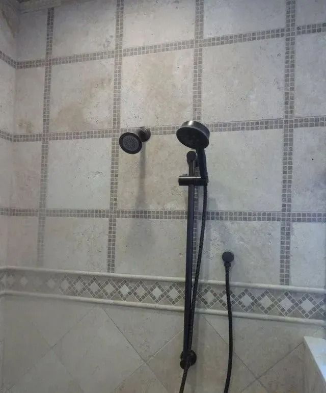 Black showerhead and handheld sprayer on a tiled bathroom wall.