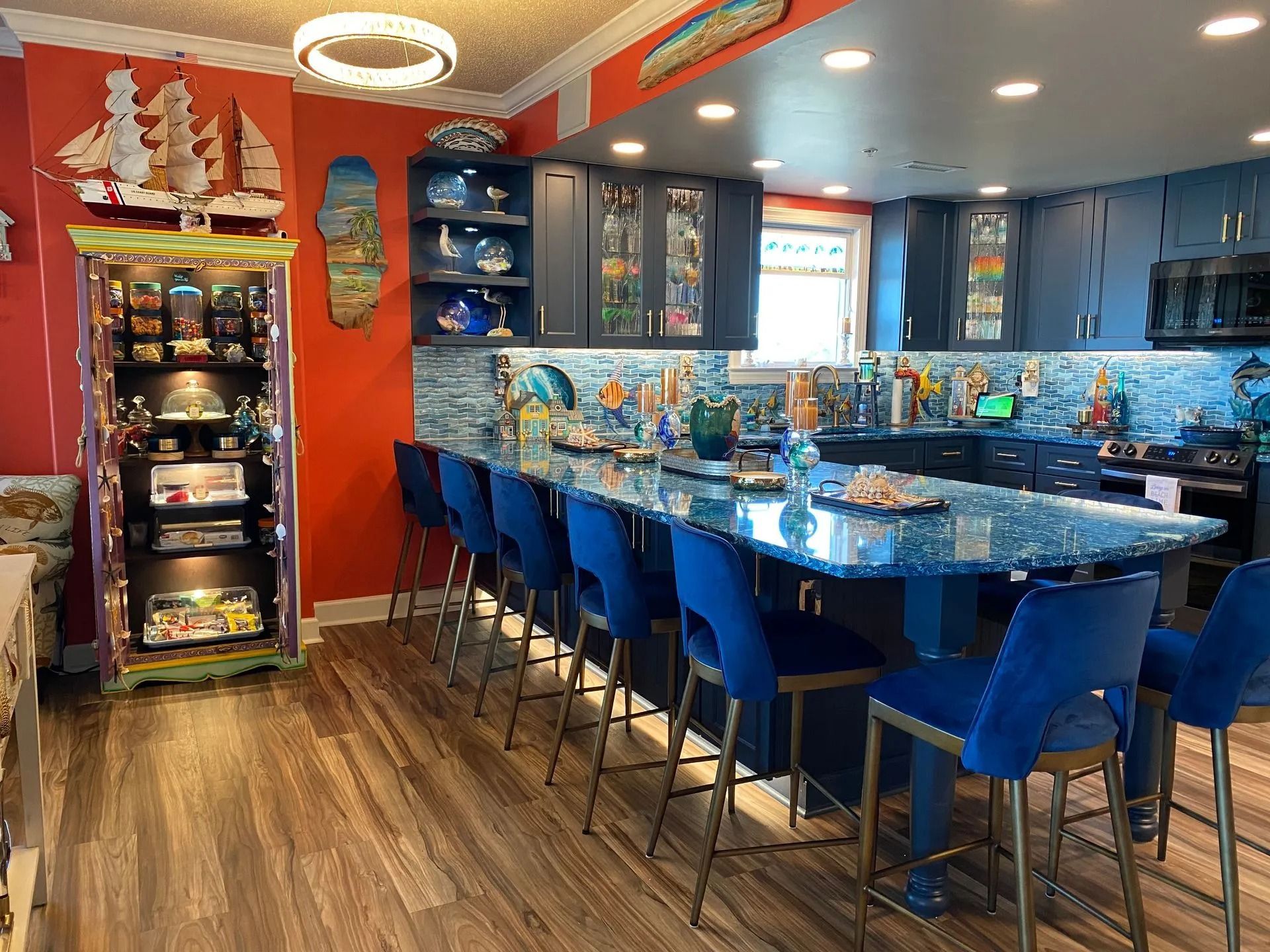 Colorful kitchen-dining room with blue bar stools, a long island, red walls, and glass cabinets