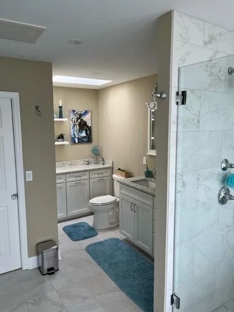 Bathroom with double vanity, toilet, blue rugs, and glass shower enclosure.