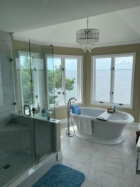 Bright bathroom with glass shower, freestanding tub, blue rug, and ocean view through windows.