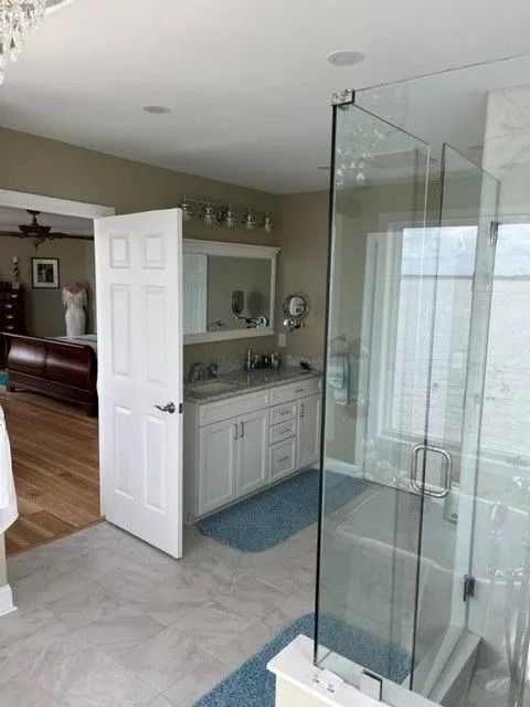 Bathroom vanity with open door, mirror, and glass shower in a bright tiled room