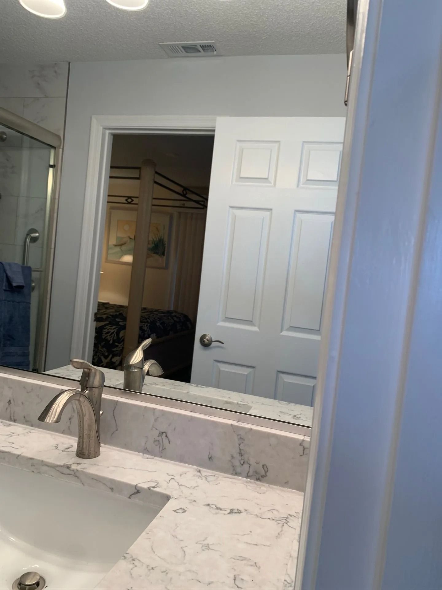 Bathroom vanity with white marble countertop, mirror, and open door reflected in the mirror