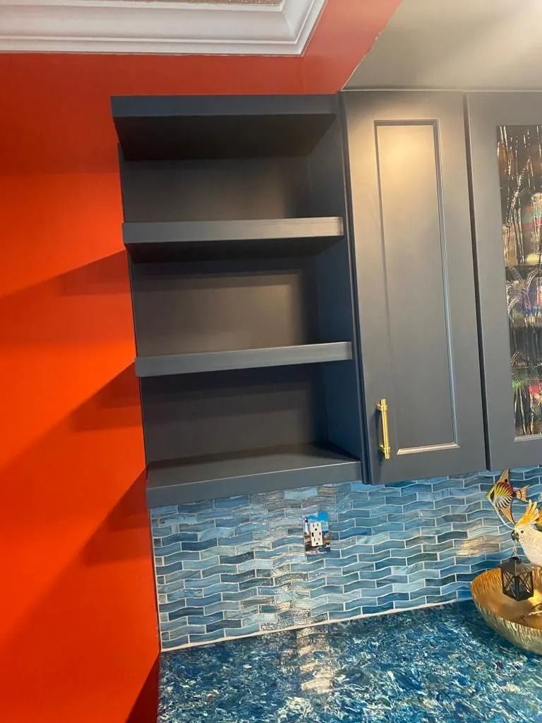 Empty black shelves set into a gray wall beside an orange wall and blue patterned countertop.