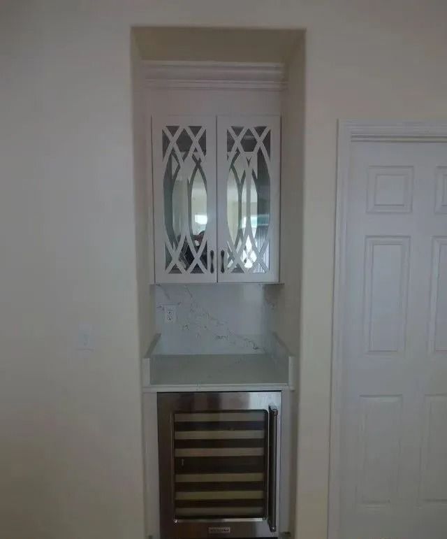 Narrow built-in cabinet with white doors and mirrored glass above a countertop, over a small under-counter fridge.