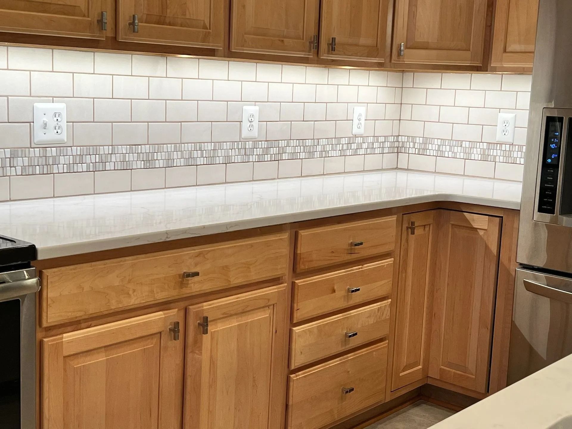 Wooden kitchen cabinets, white subway tile backsplash, and light countertop in a bright kitchen