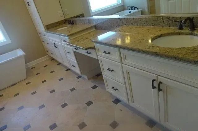Bright kitchen with white cabinets, beige countertops, and tiled floor by a sunlit window