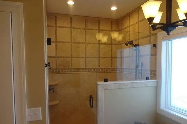 Tiled bathroom shower with glass enclosure, beige walls, and a window on the right