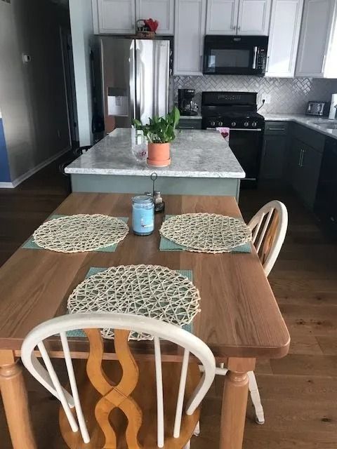 Kitchen with wooden table, woven placemats, and a potted plant on a central island.
