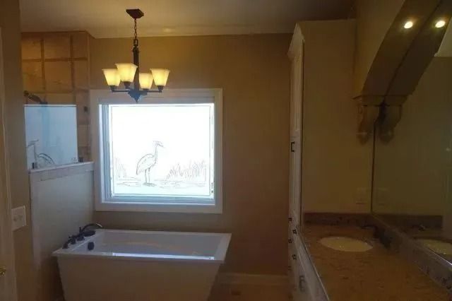 Bathroom with bathtub, window, and vanity sink under warm lighting