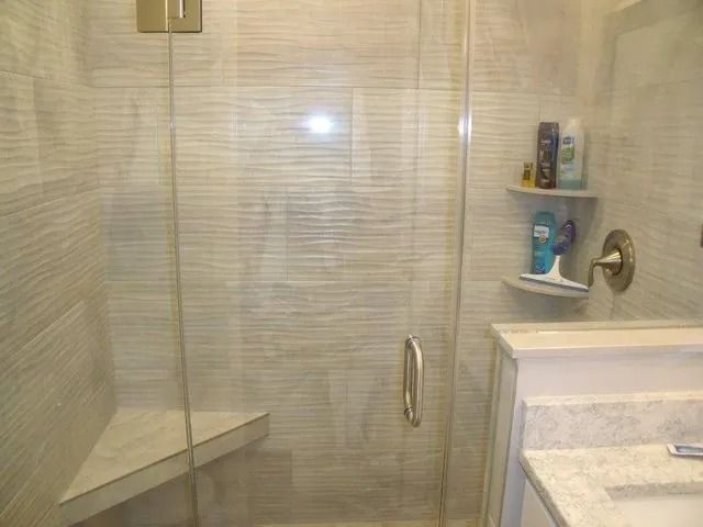 Glass-enclosed shower with beige tile, built-in corner shelf, and white vanity beside it