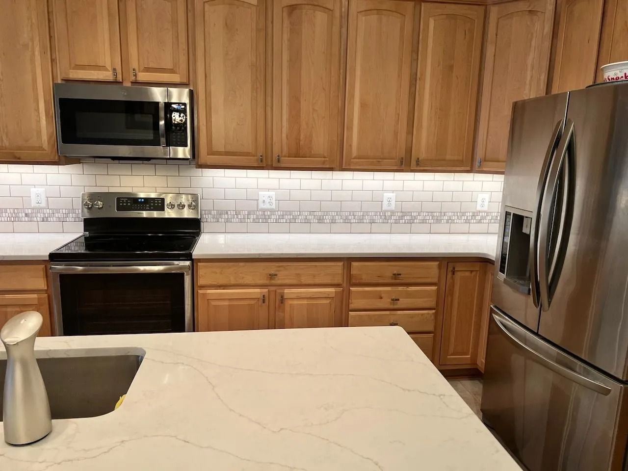 Modern kitchen with wood cabinets, stainless steel appliances, and a light countertop with sink in the foreground