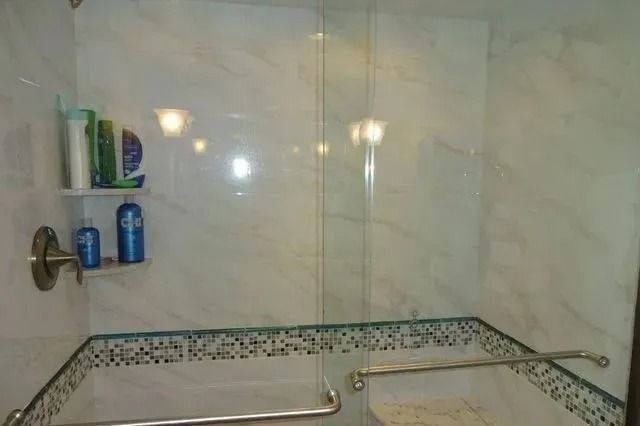 Accessible shower stall with tiled walls, grab bars, and a small corner shelf holding toiletries