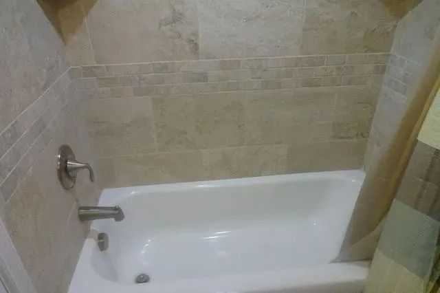 Beige tiled bathroom with a white bathtub and chrome shower fixtures
