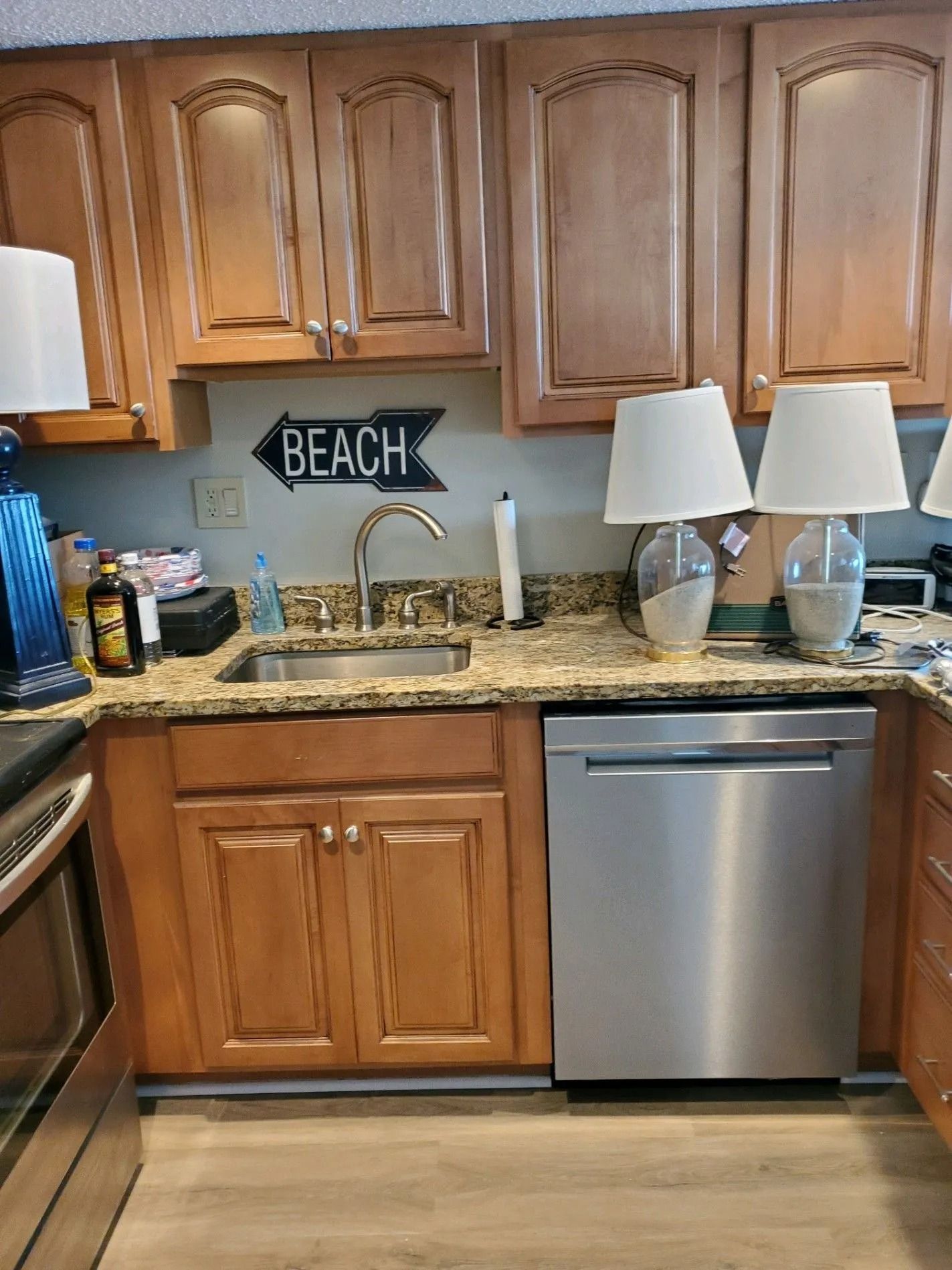 Kitchen sink under wooden cabinets with granite countertop, stainless dishwasher, and beach sign decor