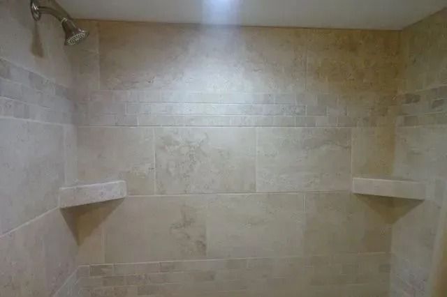 Beige tiled shower with built-in corner shelves and white ceiling