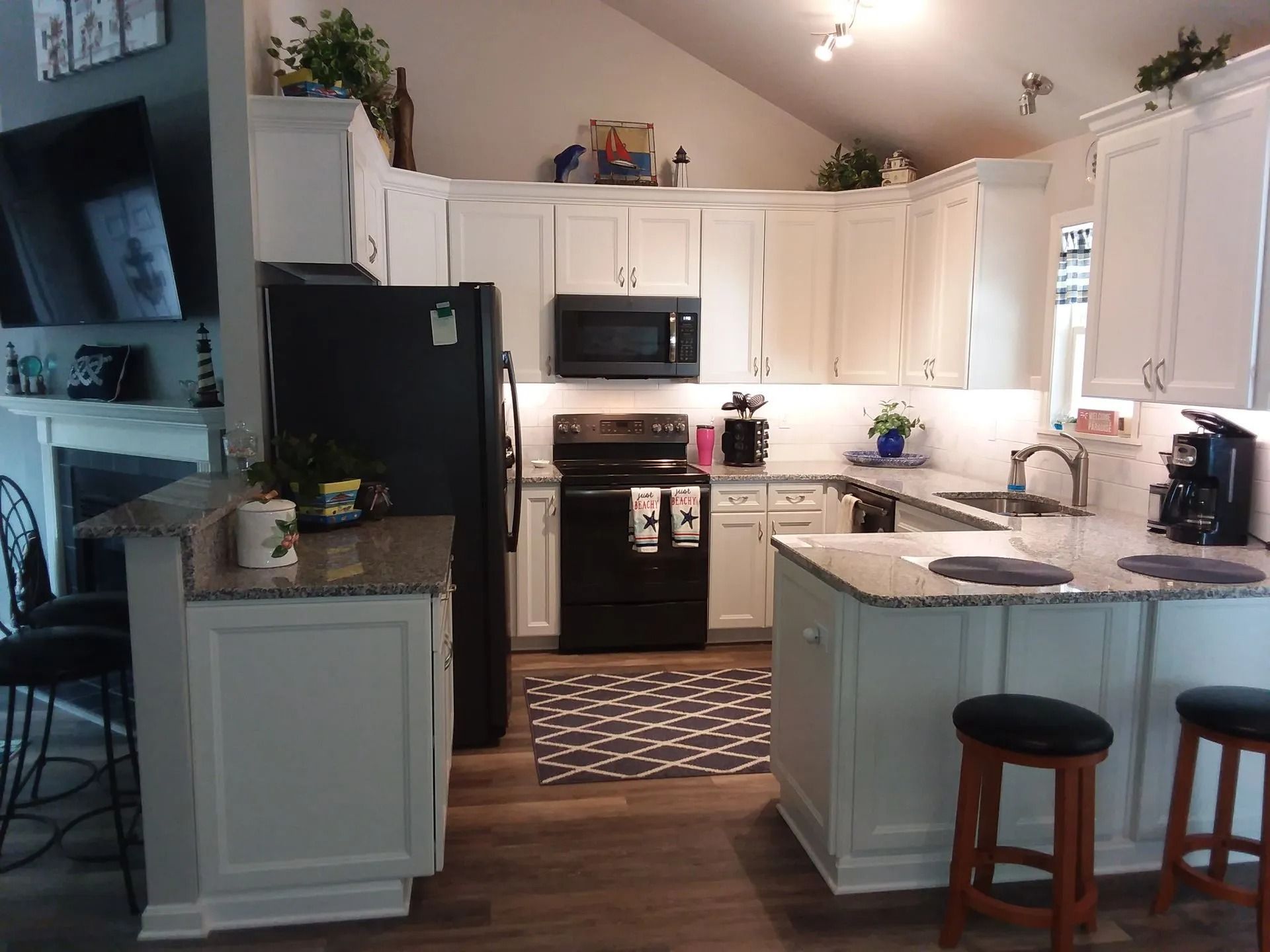 Bright white kitchen with black appliances, island, bar stools, and patterned rug under vaulted ceiling