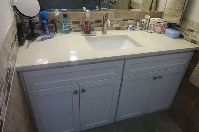 Bathroom vanity with white countertop, sink, mirror, and toiletries on the counter