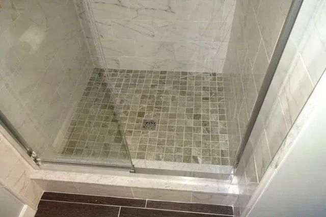 Empty tiled shower with a glass door and small mosaic floor tiles.